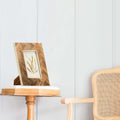 A resin and teakwood frame placed on a wooden side table in a home setting, displaying an artwork or photo.
