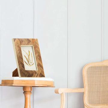 A resin and teakwood frame placed on a wooden side table in a home setting, displaying an artwork or photo.