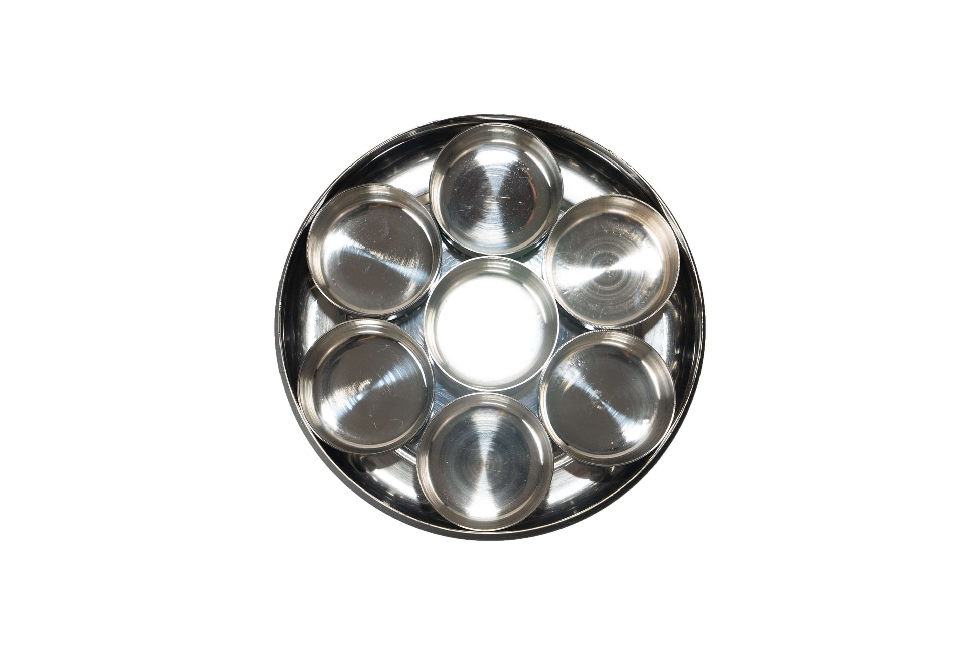 A round, seven-compartment stainless steel container, often used as a Pooja Box or spice box, shown from a top-down view on a white background. It consists of a large central container surrounded by six smaller, individual compartments.