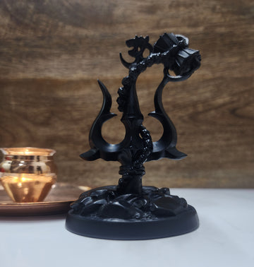 A black statue featuring a Shiva Trishul with a Damaru (drum) attached, and an Om symbol at its peak, all set on a dark, textured base.