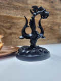 A black matte finished figurine of a Lord Shiva's Trishul (trident) with an attached Damru (drum) on a round base.