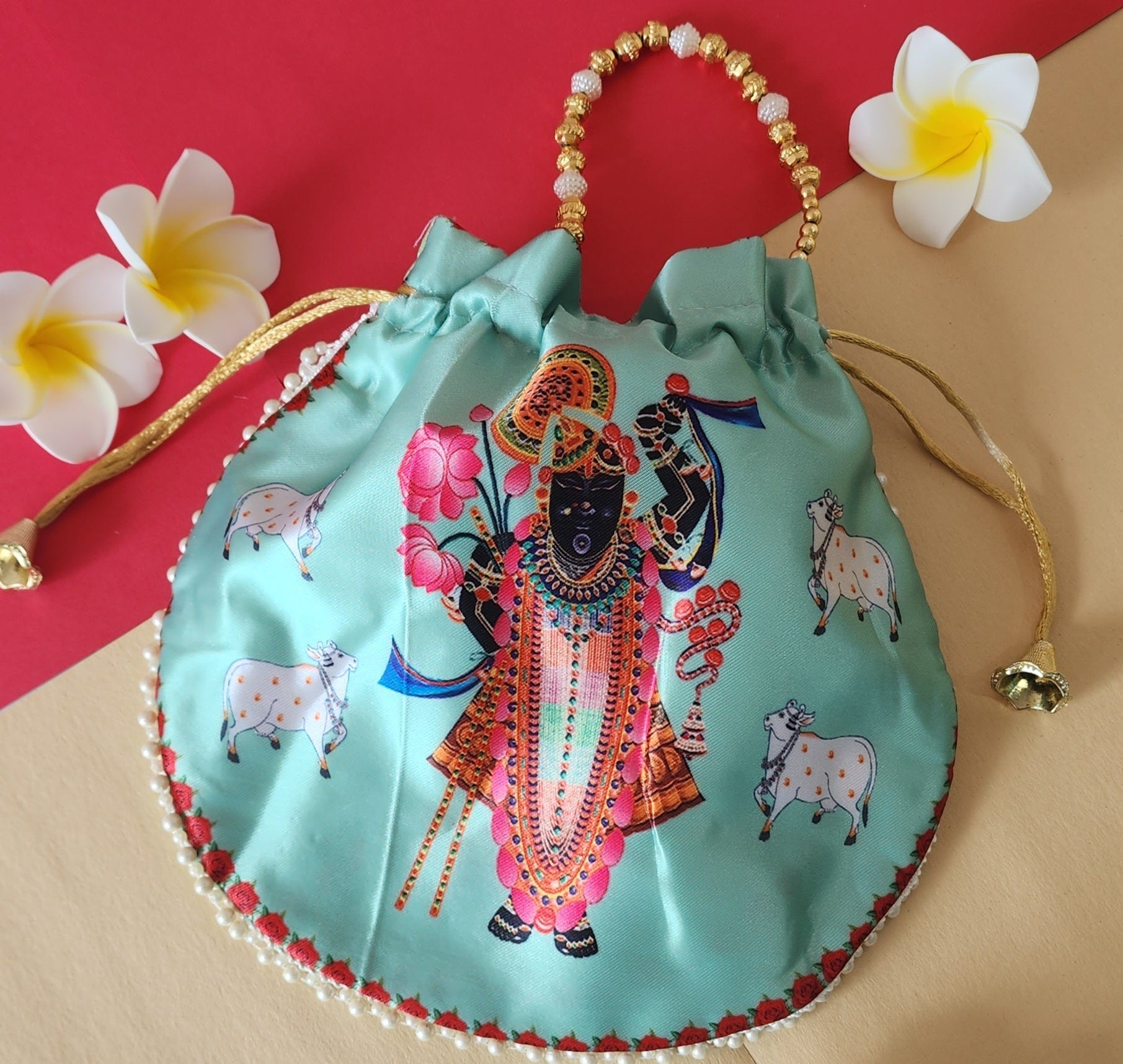 A light green Shreenathji Potli Bag featuring a printed image of Lord Krishna surrounded by cows, with a beaded handle and pearl trim.