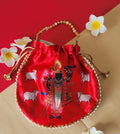 A vibrant red potli bag with a printed image of Shreenathji and cows, accented with a beaded handle and surrounded by white and yellow frangipani flowers, all set against a red and beige background.