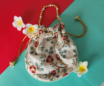 A beige potli bag with a floral printed design, displayed against a two-tone background with yellow flowers on the side.