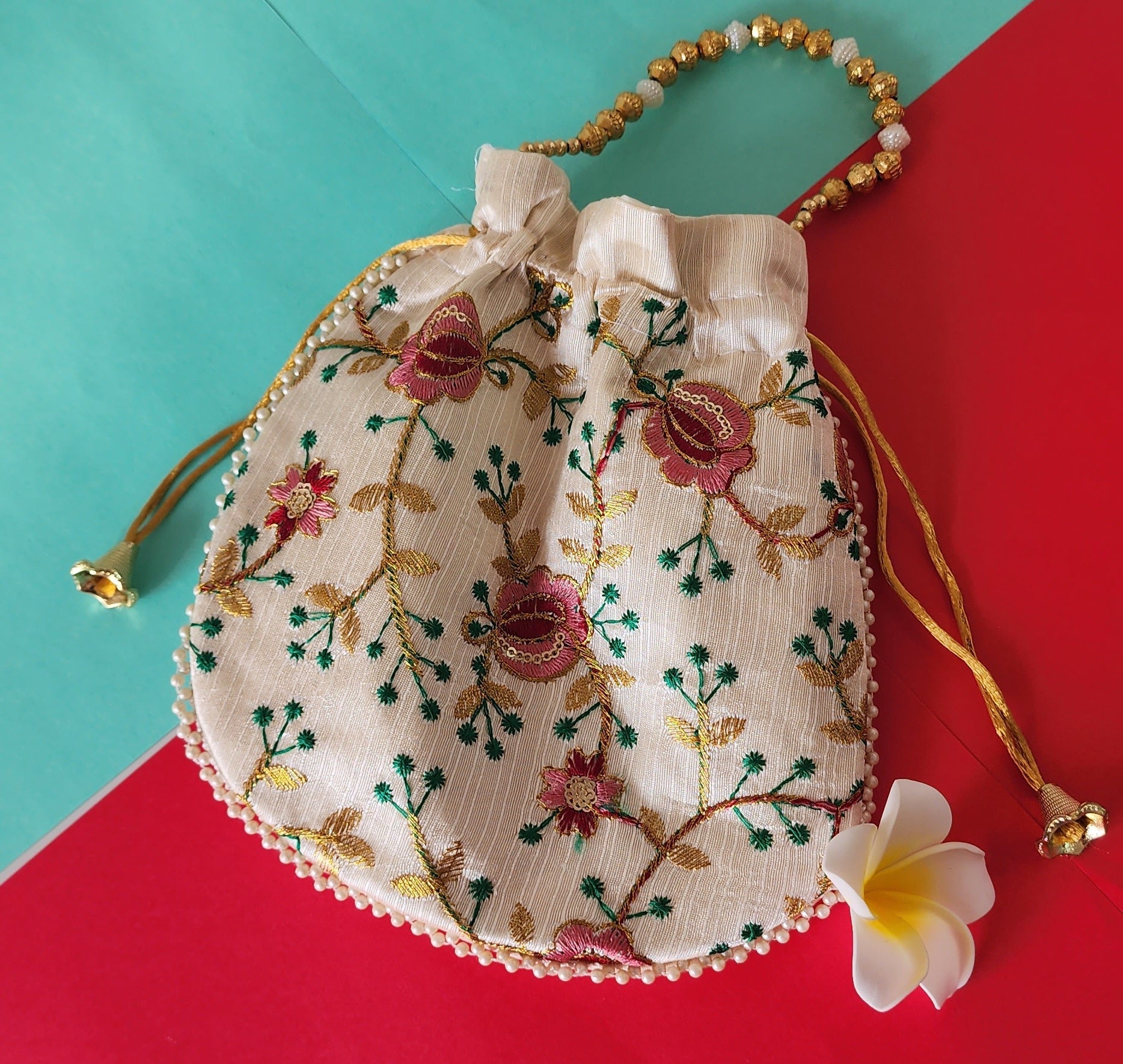 A beige potli bag with a floral printed design, displayed against a two-tone background with yellow flowers on the side.