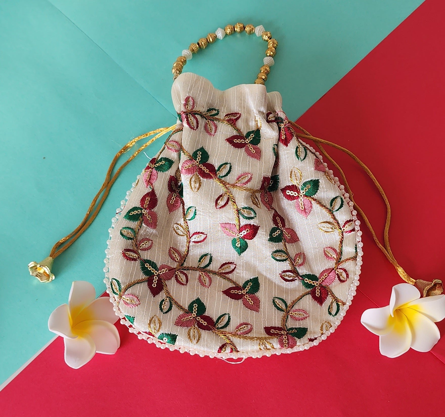 A beige potli bag with a floral printed design, displayed against a two-tone background with yellow flowers on the side.