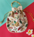 A beige potli bag with a floral printed design, displayed against a two-tone background with yellow flowers on the side.