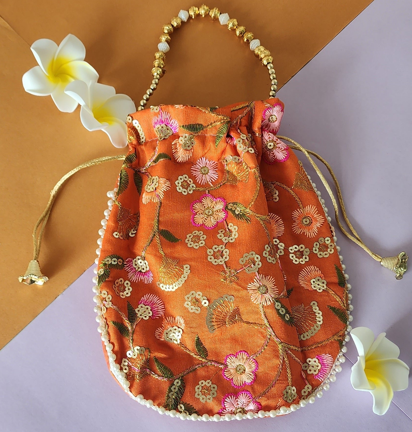 A Orange floral design potli bag with golden embroidery and a drawstring closure