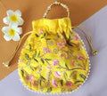 A yellow floral design potli bag with golden embroidery and a drawstring closure, displayed alongside yellow flowers.