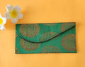 A green envelope with traditional block print patterns displayed on a yellow background, accompanied by a white flower with a yellow pistil.