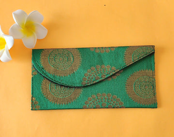 A green envelope with traditional block print patterns displayed on a yellow background, accompanied by a white flower with a yellow pistil.