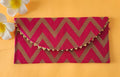 A V-shaped red and gold shagun envelope with a zigzag pattern and decorative golden trimmings, displayed on an orange background with a frangipani flower beside it.