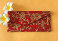 A red envelope with gold floral embroidery, placed on an orange surface with two white flowers at the top left corner.