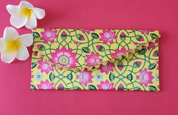 A multicolored floral patterned Designer Shagun Envelope placed on a pink surface with two white flowers at the top left corner.