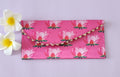 A multicolored floral patterned Designer Shagun Envelope placed on a pink surface with two white flowers at the top left corner.