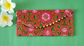 A multicolored floral patterned Designer Shagun Envelope placed on a pink surface with two white flowers at the top left corner.