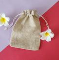A beige Potli gift bag with a drawstring closure, with flowers around it