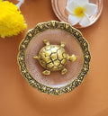 A decorative ceramic bowl in pastel pink color with intricate gold patterns around the rim, containing a small turtle figurine with a detailed, earthy-toned shell.