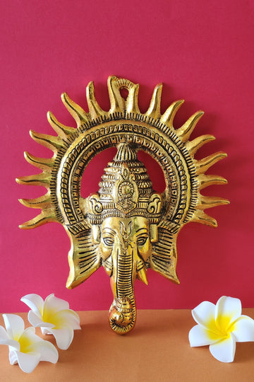 Brass Ganesha Wall Hanging standing on the pink wall and white flowers around it
