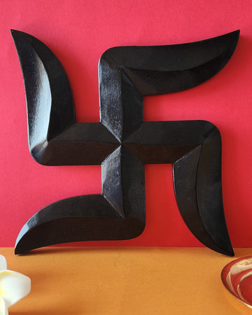A black Swastik wall decor art hanging on a red background, representing auspiciousness and good luck.