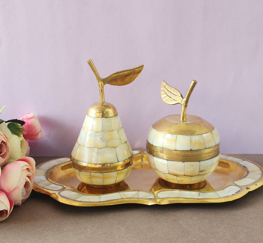 A decorative brass set featuring apple and pear shaped containers with tray, inlaid with mother of pearl, displayed against a pink background.