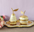 A decorative brass set featuring apple and pear shaped containers with tray, inlaid with mother of pearl, displayed against a pink background.