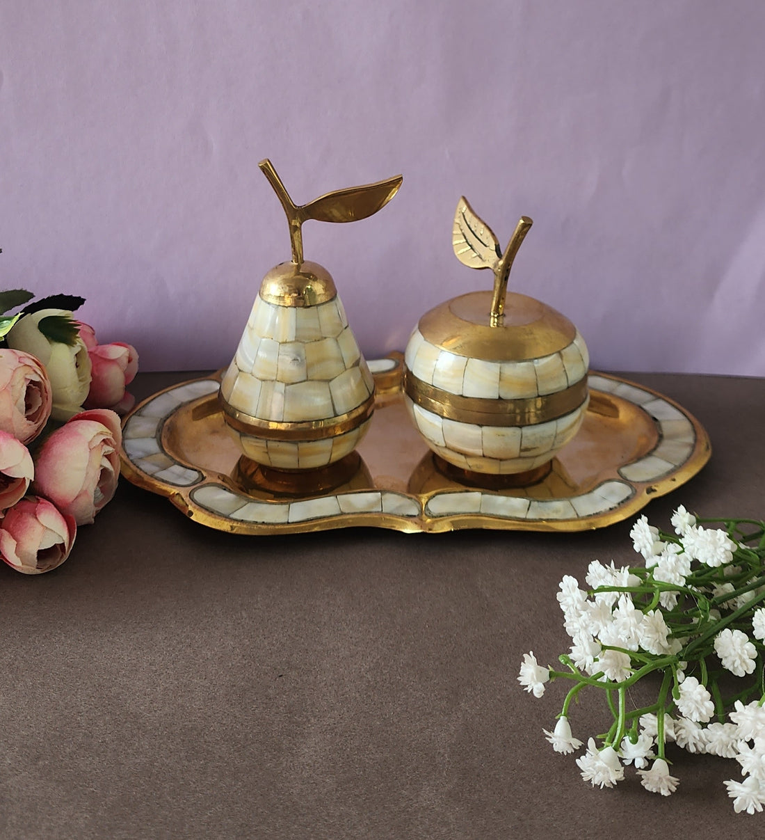 A decorative brass set featuring apple and pear shaped containers with tray, inlaid with mother of pearl, displayed against a pink background.