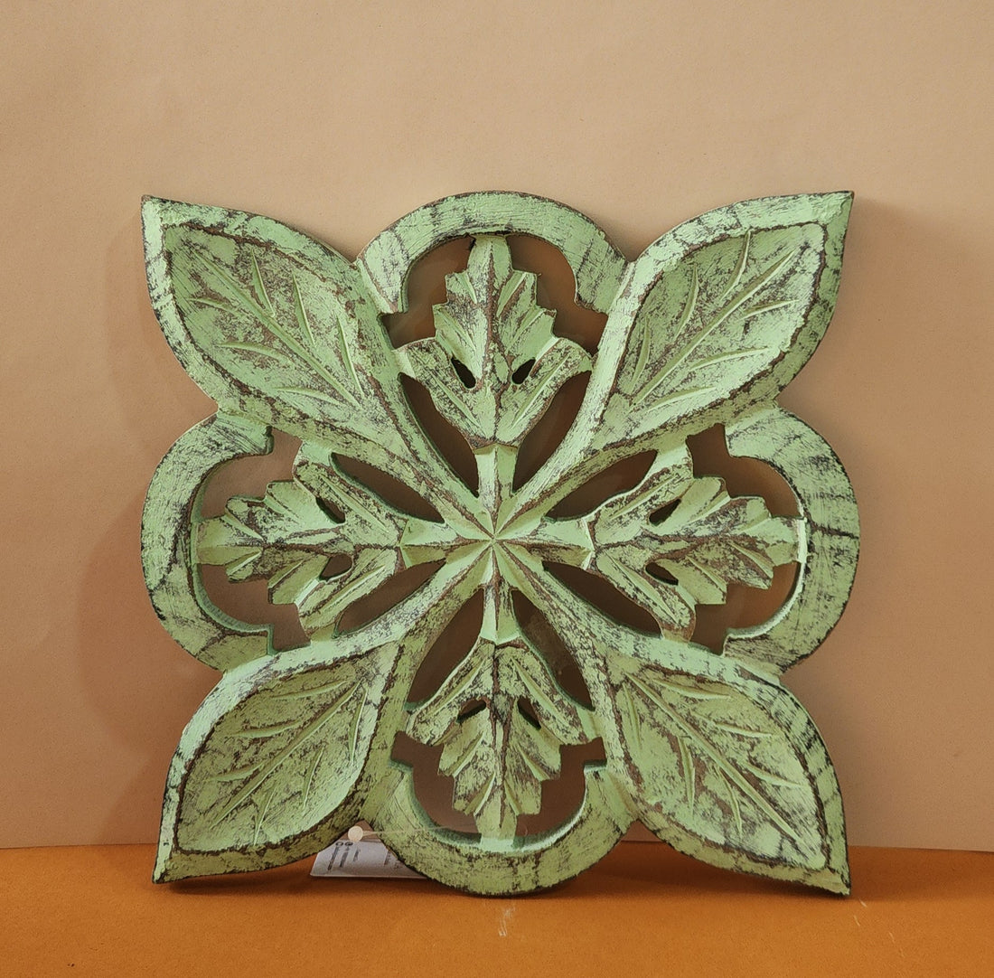 A wooden carved trivet with a green finish, featuring intricate leaf patterns.