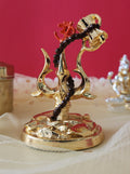 A detailed image of a golden Trishul, the trident of Lord Shiva, featuring a damru (drum) tied to its center and an 'Om' symbol at the top of the handle, resting on a golden base.