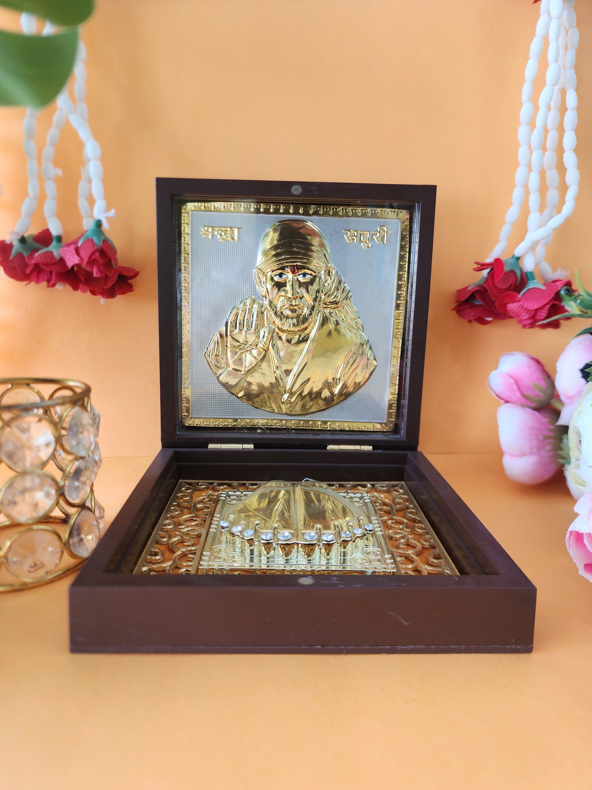A decorative wooden box containing a golden plaque with an image of Shirdi Sai Baba and a set of golden Charan Paduka (sacred footprints).