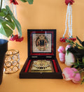 A beautifully presented Ram Lalla Pocket Temple, featuring a framed image of Lord Ram and Charan Paduka, housed in a decorative wooden box, surrounded by flowers, garlands, and a sparkling candle holder, set against an orange backdrop.