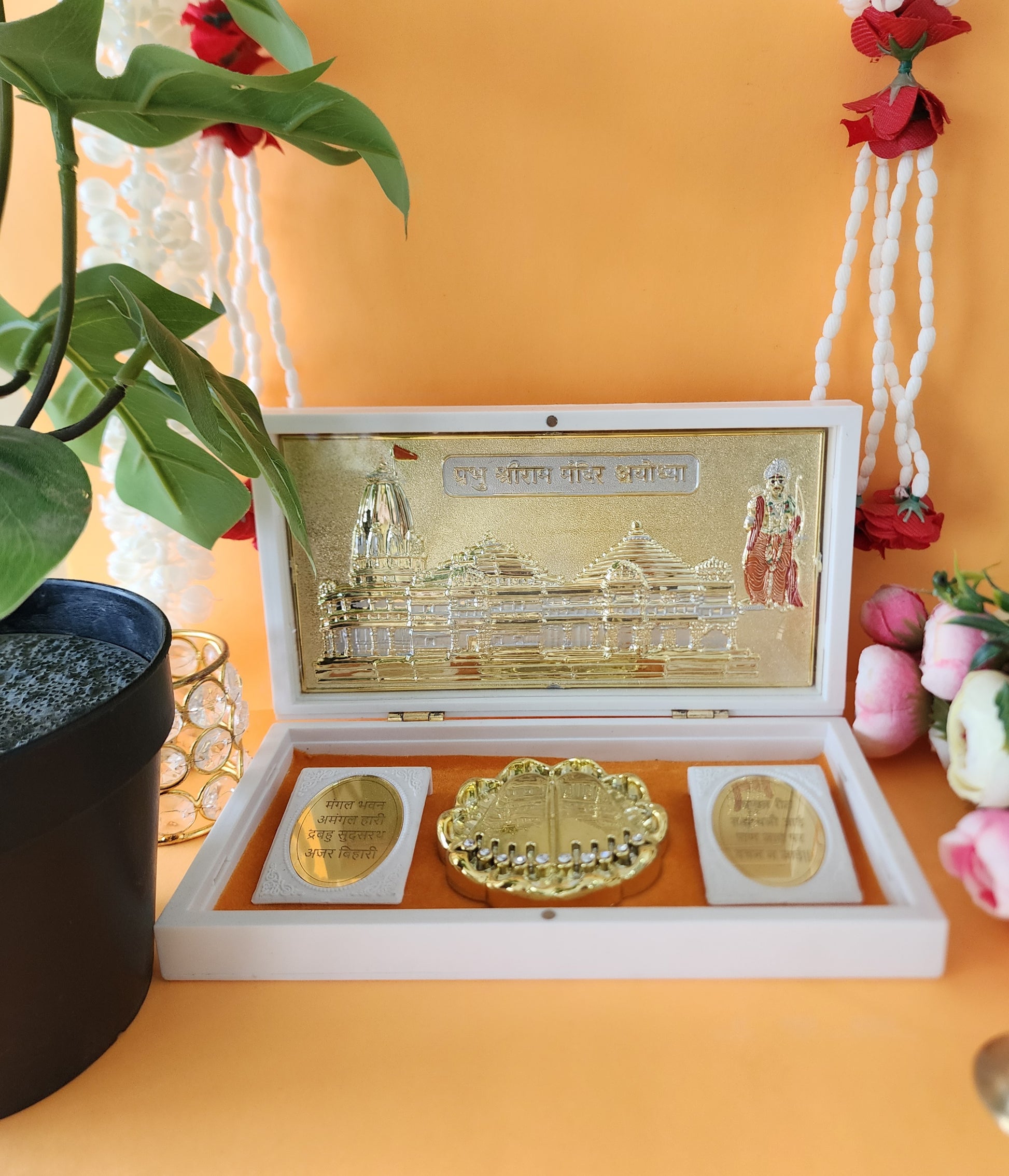 Close-up of a white box containing a golden Shree Ram Mandir replica, along with two inscribed plates and a central Charan Paduka.
