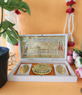 An elegant white box open to display a detailed, gold-plated miniature of the Ayodhya Ram Temple with accompanying spiritual symbols.