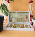 Decorative white box with a golden Shree Ram Mandir replica and Lord Ram's Charan Paduka, placed on a beige surface with floral decorations.