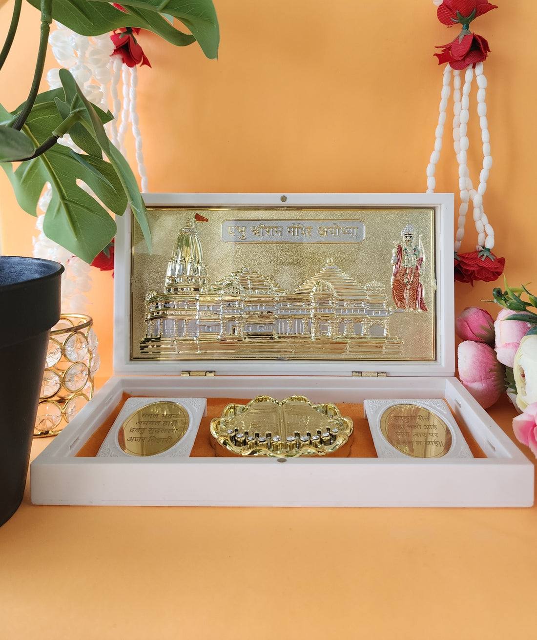 White, open decorative box revealing a gold-plated miniature of the Ayodhya Ram Mandir and sacred Charan Paduka inside.