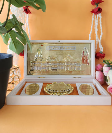 White, open decorative box revealing a gold-plated miniature of the Ayodhya Ram Mandir and sacred Charan Paduka inside.
