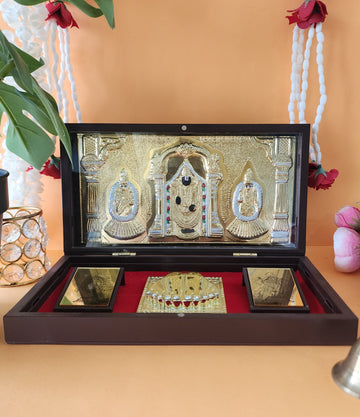 A gold-plated Balaji Laxmi Padmavati Pocket Temple featuring Lord Balaji in the center with Goddess Lakshmi and Padmavati on either side, placed inside a brown wooden box lined with red velvet, accompanied by golden Charan Paduka and other miniature religious elements.