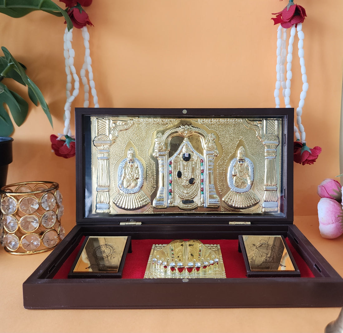 A gold-plated Balaji Laxmi Padmavati Pocket Temple featuring Lord Balaji in the center with Goddess Lakshmi and Padmavati on either side, placed inside a brown wooden box lined with red velvet, accompanied by golden Charan Paduka and other miniature religious elements.