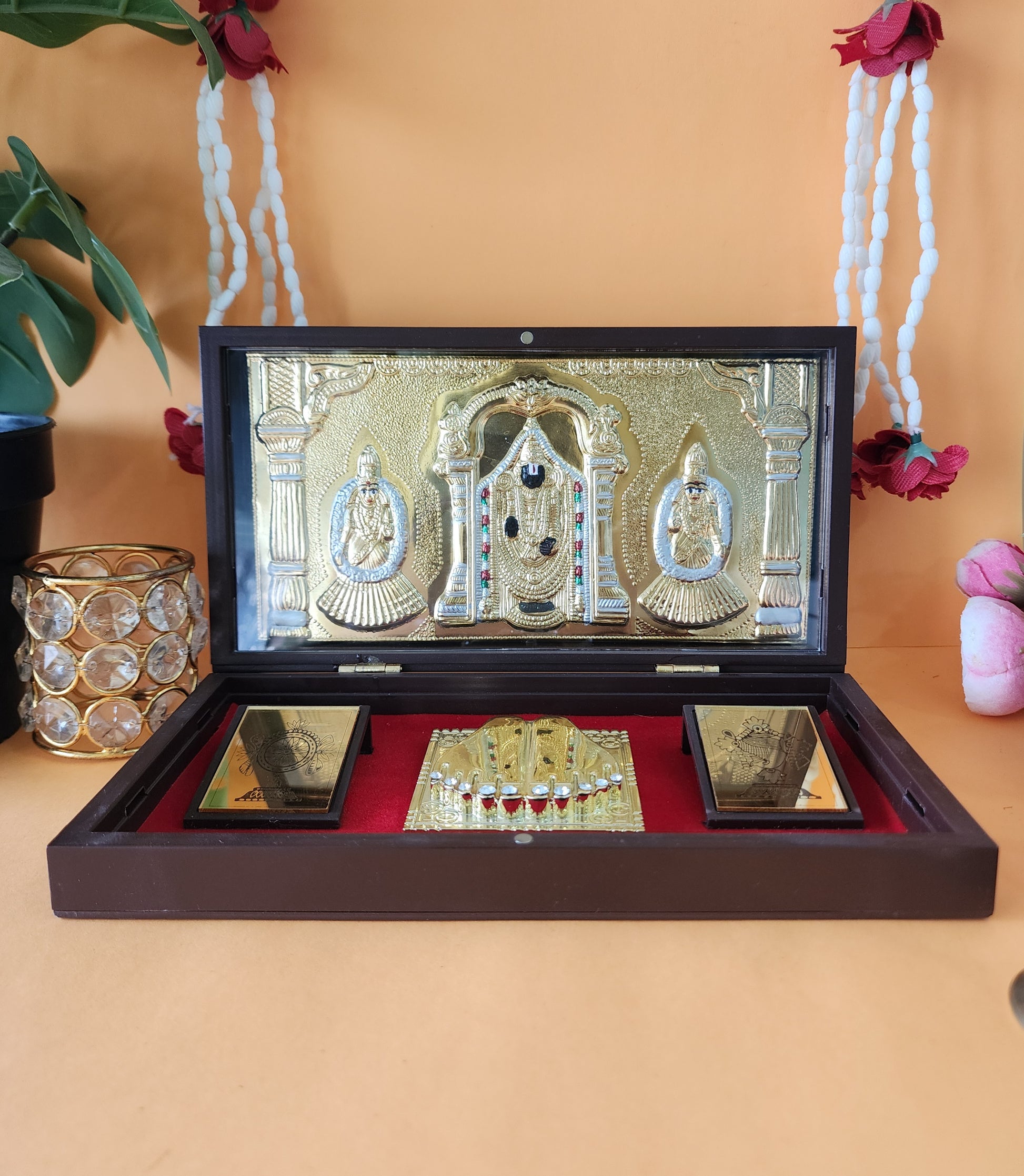 A gold-plated pocket temple featuring Lord Balaji, Goddess Lakshmi, and Goddess Padmavati, along with Charan Paduka, housed within a wooden framed box.