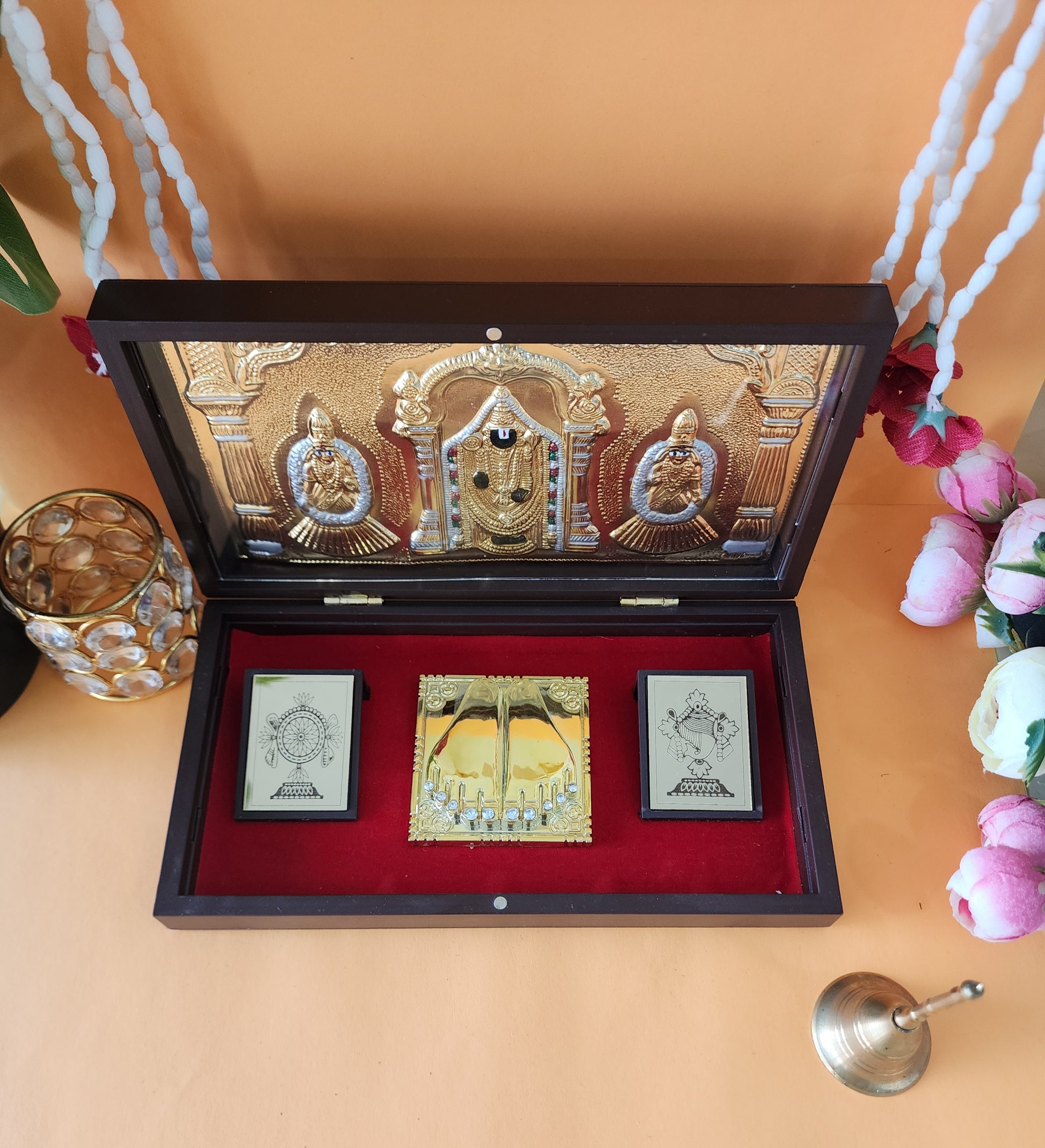 An open ornate wooden box lined with red velvet, displaying a gold-plated image or idol of Lord Tirupati Balaji flanked by Lakshmi and Padmavati, along with gold-plated symbolic representations of Shankha, Chakra, and Charan Paduka (divine feet) on a black base.