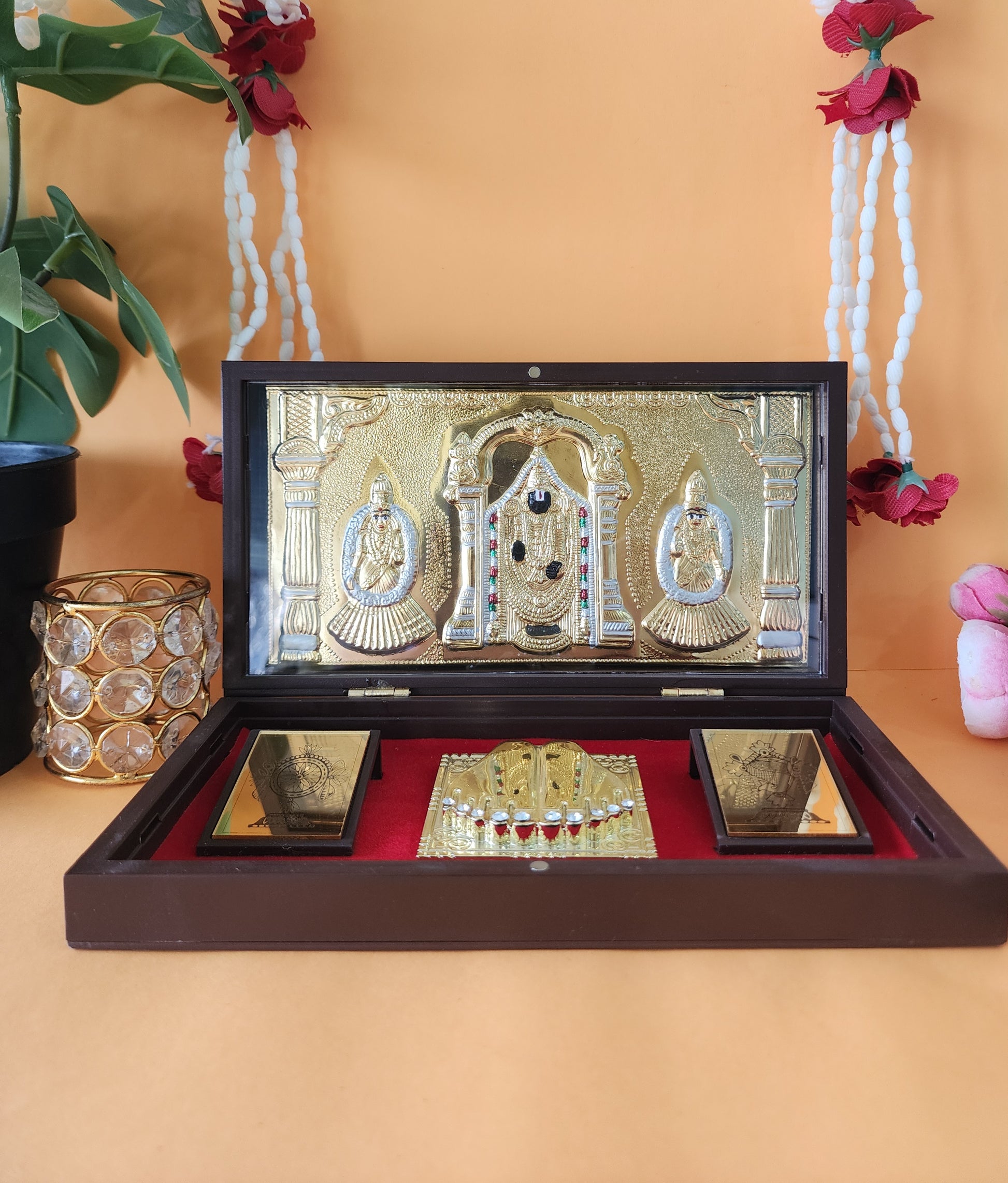 A detailed image of a Lord Balaji, Laxmi, and Padmavati pocket temple, featuring gold-plated deities and auspicious symbols like Shankha, Chakra, and Padalu, enclosed within a decorative wooden box with a magnetic lock, commonly used for travel, home altars, or gifting during religious occasions.