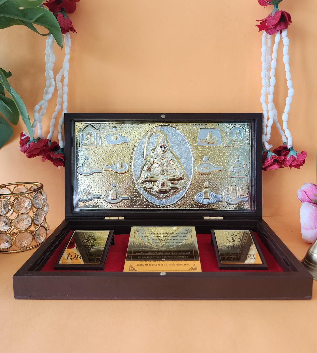 A gold-plated Lord Shiva Pocket Temple, featuring a central idol surrounded by smaller deities or symbols, displayed in an open wooden box with a red velvet interior and two additional gold-colored plaques with "Om" symbols.