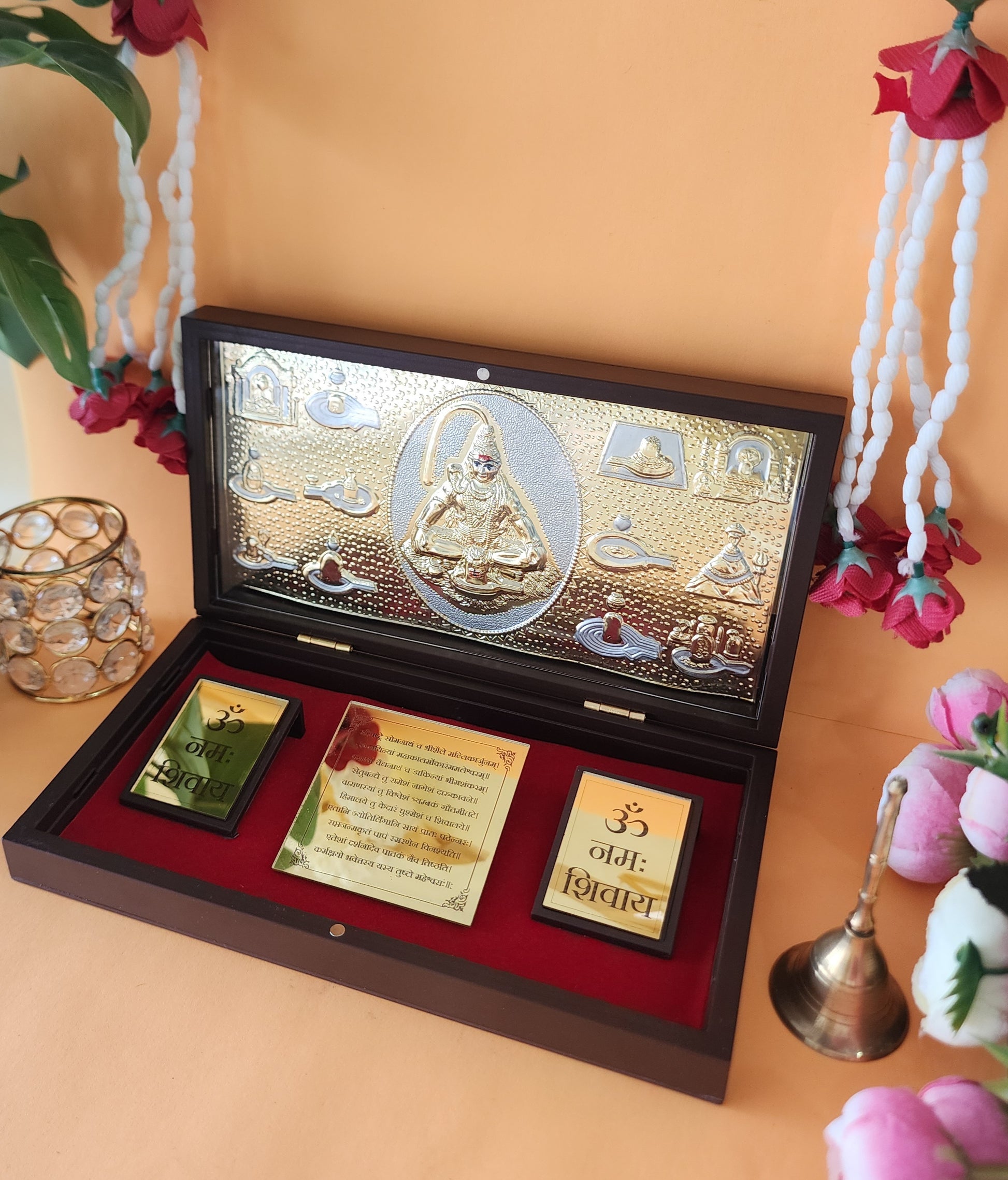 A decorative wooden box with a gold-toned interior featuring an embossed image of Lord Shiva and other deities, alongside smaller golden plaques inscribed with "ॠनमः शिवाय" in Devanagari script, possibly a puja box or pocket temple.