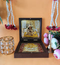 A portable Swami Samarth Pocket Temple, featuring a gold-plated idol of Swami Samarth and Charan Paduka housed within a dark wooden box, surrounded by traditional Indian garlands and flowers against an orange background.