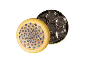 A peacock yellow Pooja Box (5inch) with a lid decorated with a colorful, intricate peacock feather mandala design. The round box is shown open, revealing a stainless steel container inside with seven smaller circular compartments for storing items.