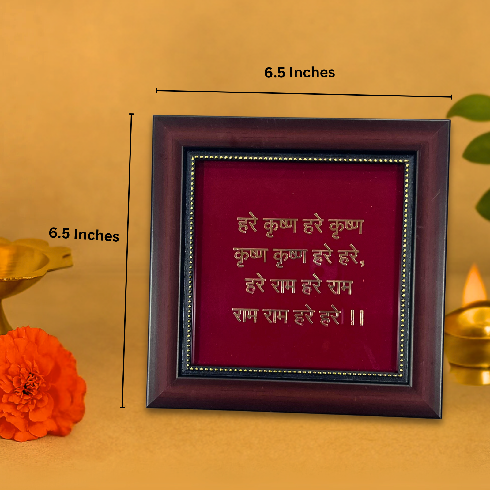 A wooden-framed photo print of the Hare Krishna Mahamantra on a red background, measuring 6.5 inches by 6.5 inches, with a small brass pot and a marigold flower visible in the soft-focus foreground on the left. The gold Devanagari script on the frame reads: "Hare Krishna Hare Krishna Krishna Krishna Hare Hare, Hare Rama Hare Rama Rama Rama Hare Hare.