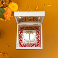 Lord Balaji Charan Paduka, a sacred footprint symbol of Lord Venkateswara, displayed in a white, ornate box on an orange background with marigold flowers and petals.