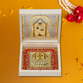 An open white wooden box-temple revealing gold-plated religious artifacts inside. The upper compartment displays a framed image of Lord Tirupati Balaji, while the lower compartment showcases the gold-plated Charan Paduka (divine footprints) of Lord Balaji on a vibrant red background with intricate golden designs.