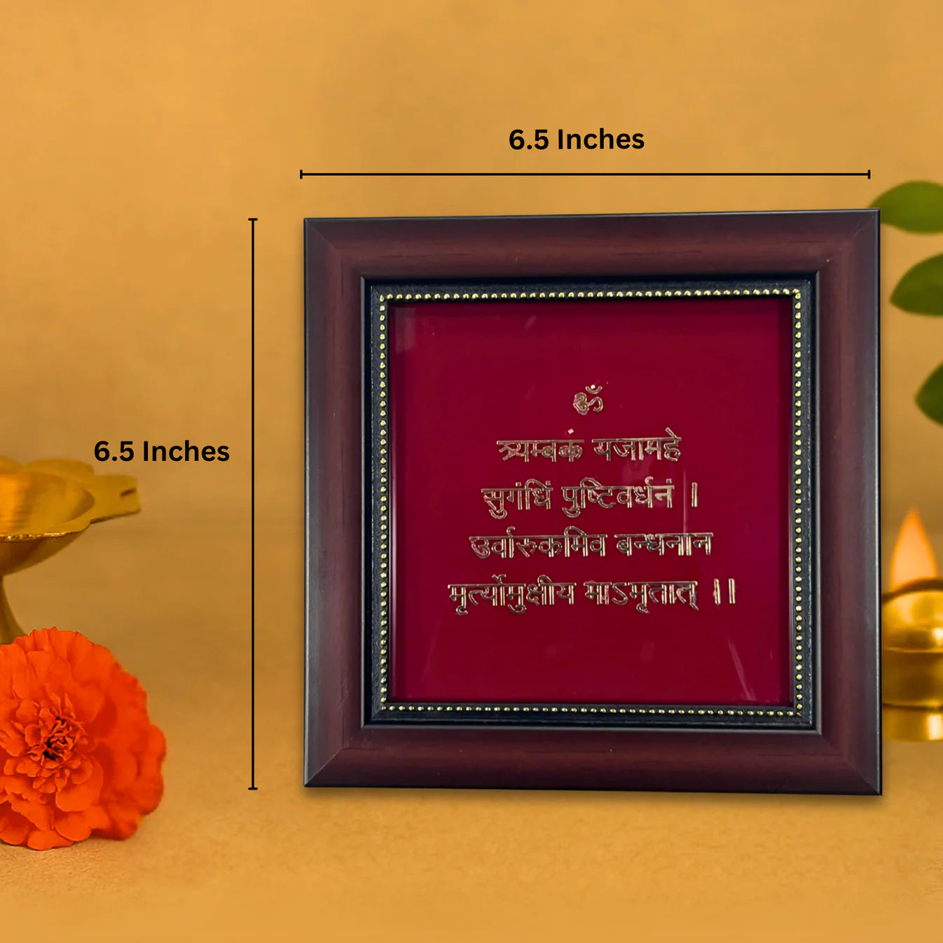 A brown wooden photo frame with a deep red backing contains the Mahamrityunjaya Mantra in gold-colored Sanskrit script. The mantra, which is dedicated to Lord Shiva, is visible in the center of the frame. The frame measures 6.5 inches by 6.5 inches, as indicated by text and dimension lines.