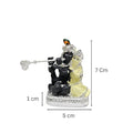 A small, black and yellow idol depicting Radha and Krishna, with dimensions labeled as 7 cm (height), 5 cm (width), and 1 cm (base thickness).